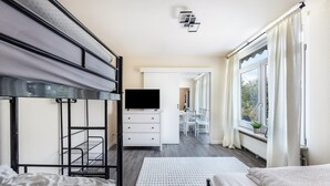 Un dormitorio con camas literas, un televisor de pantalla plana, un aparador blanco y vistas a un comedor a través de una puerta.