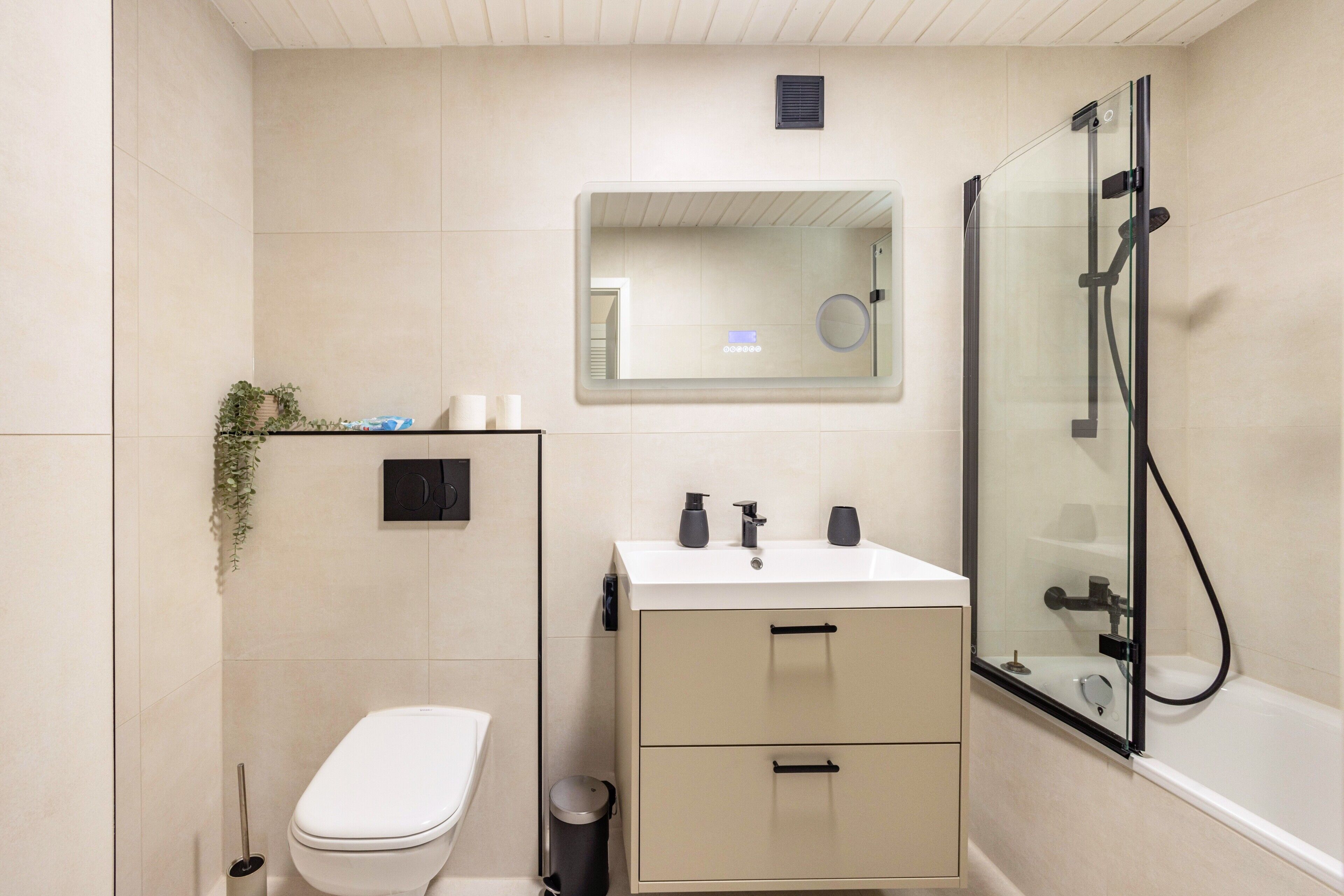 A bathroom with a toilet, sink, mirror, and glass-enclosed shower.