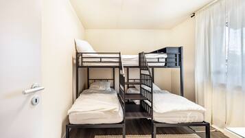 Habitación con literas, una puerta, una ventana con cortinas y una lámpara en el techo.