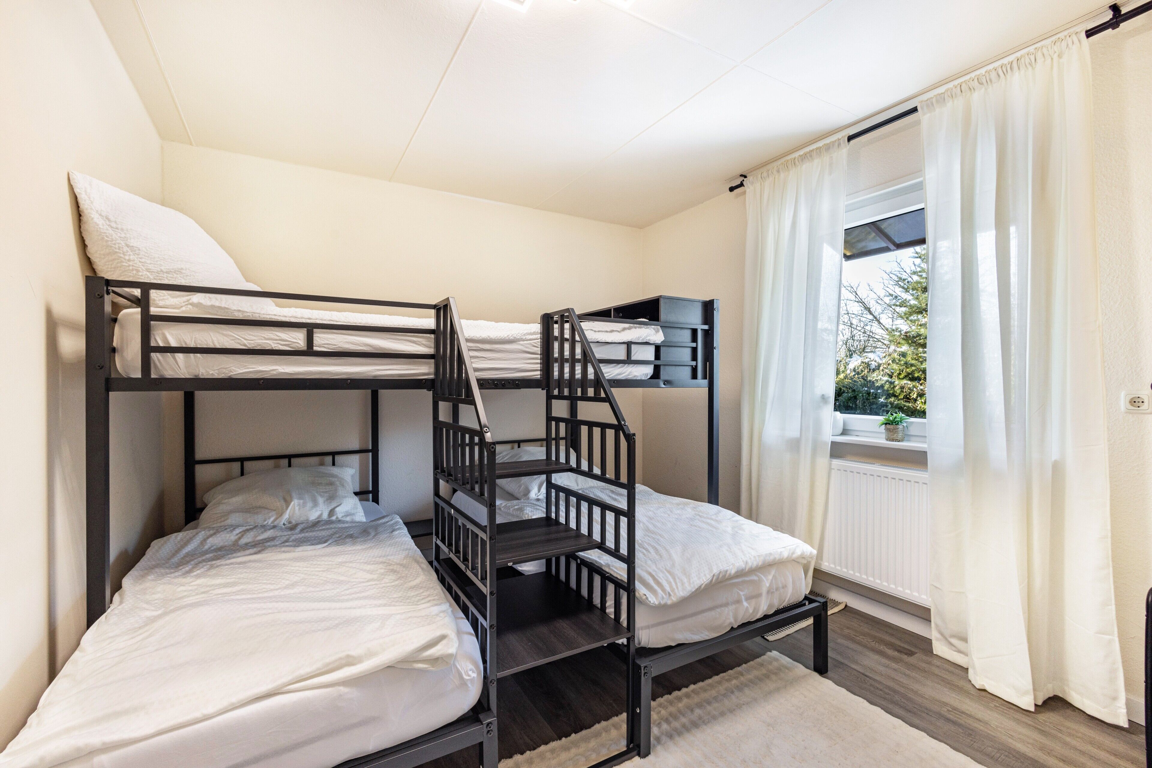 Een slaapkamer met een stapelbed, raam, gordijnen en een radiator.