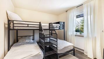 Een slaapkamer met een stapelbed, raam, gordijnen en een radiator.