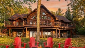Eine Blockhütte mit Feuerstelle und roten Adirondack-Stühlen davor.