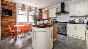 A modern kitchen with white cabinets, a wooden dining table with orange chairs, and a built-in oven. - Main Street (No 115) | Lower Largo (Lower Largo)