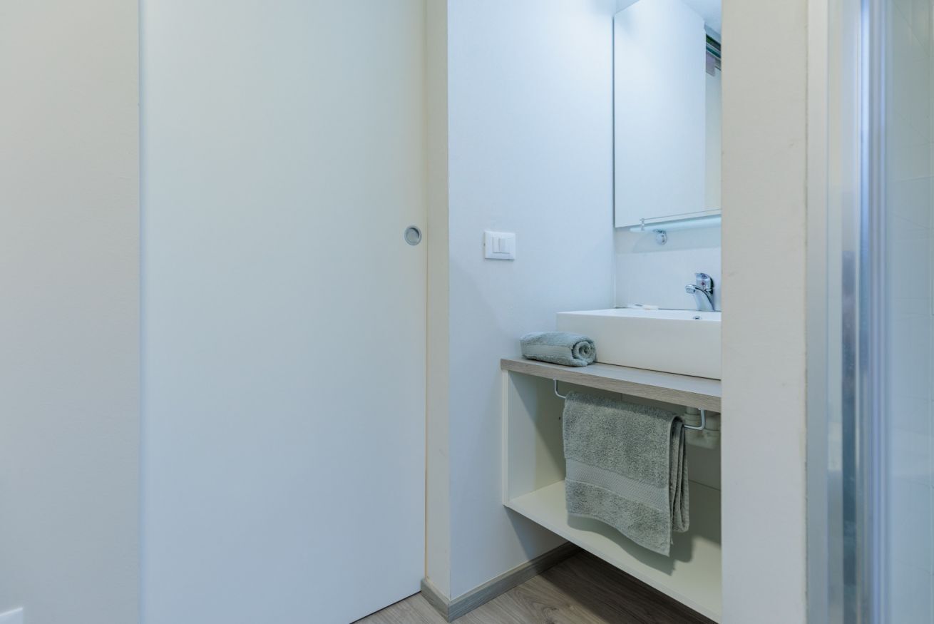 Een kleine, schone badkamer met een witte wastafel, een spiegel en een handdoek aan een rek.