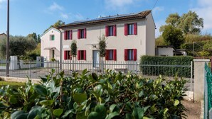 A two-story building with red shutters, a white facade, and a small front garden. - The property is located in a strategic position: a 7-minute walk from the international barracks, 5 minutes by car from the town center, 5 minutes by car from the hospital, and just 30 seconds from the riverside along the Livenza, perfect for cycling.Ava (Riva Livenza)