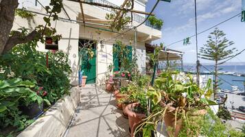 Un balcón con plantas en macetas, vista al mar y un edificio con un letrero.
