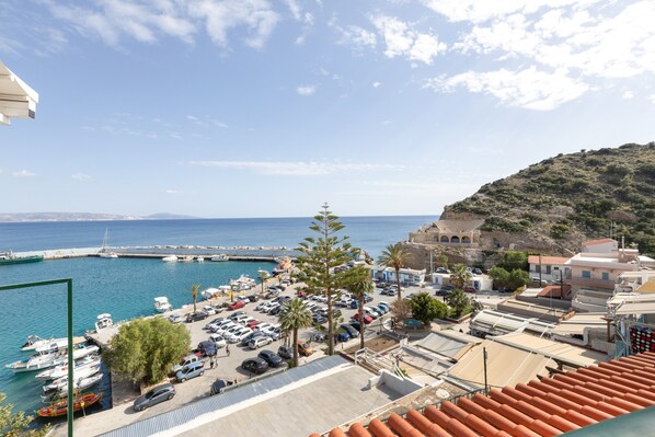 Un port de plaisance situé sur la côte, où l’on peut voir des voitures garées, des bateaux et des bâtiments à l’architecture méditerranéenne.