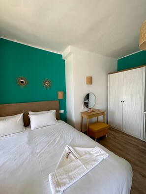 Une chambre d’hôtel avec un lit, une table de chevet en bois, un miroir et une armoire.