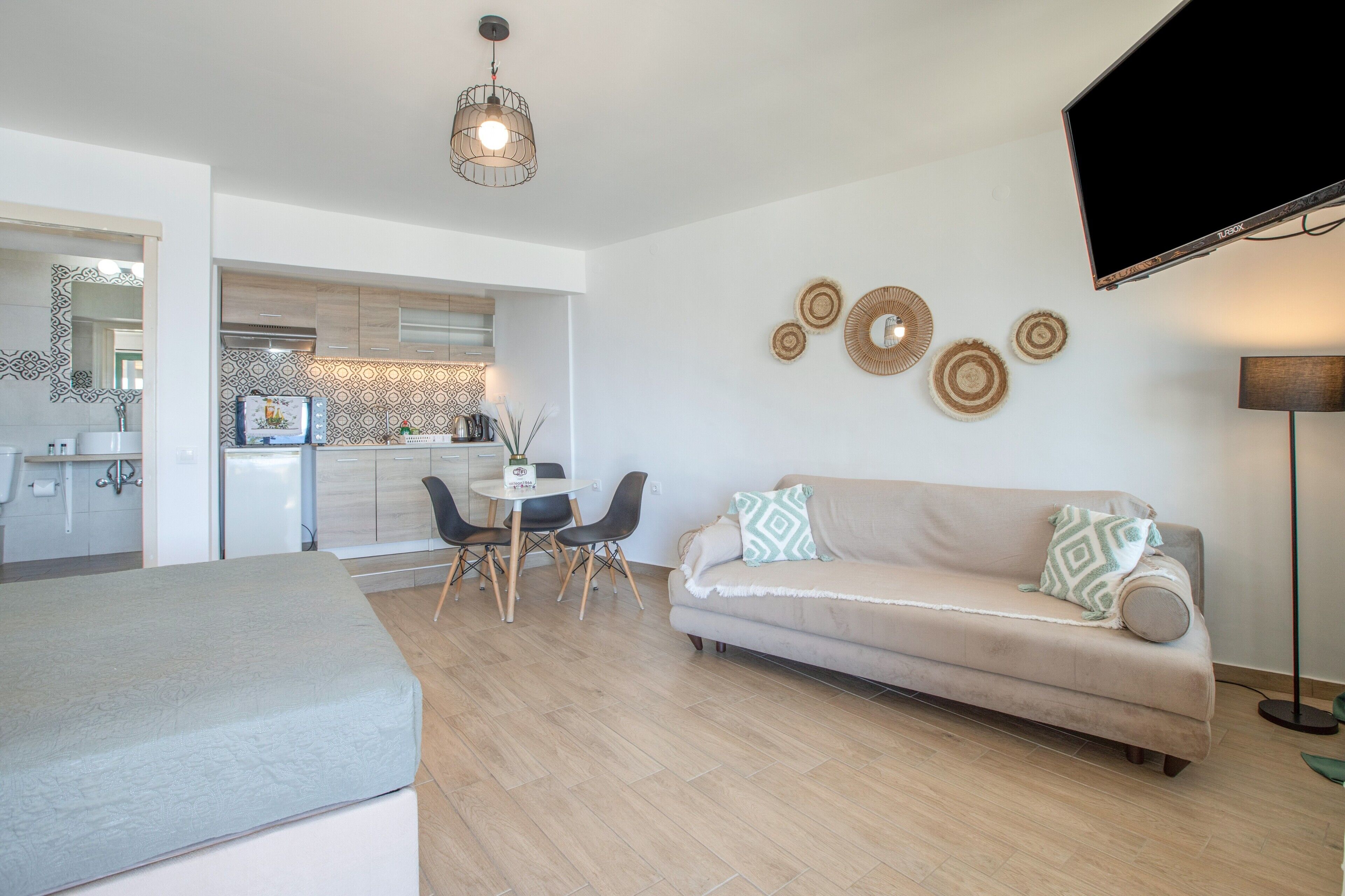 Un salon moderne comprenant un canapé, une table à manger avec des chaises, un coin cuisine et un téléviseur à écran plat fixé au mur.
