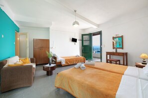 A hotel room with two beds, a sofa, a desk, a TV, and a view of the sea.