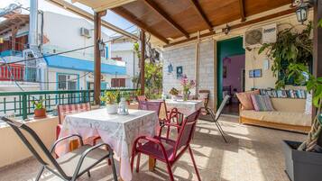 Un patio al aire libre con mesas y sillas, un sofá, plantas en macetas y vistas de los edificios circundantes.