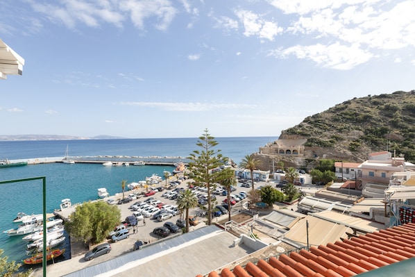 Un port de plaisance situé sur la côte, où l’on peut voir des voitures garées, des bateaux et des bâtiments à l’architecture méditerranéenne.