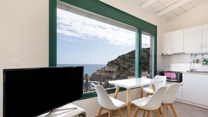 A modern kitchen with white cabinets, a dining area with white chairs, a flat-screen TV, and a view of the sea. - Apartment 'Two Bedroom  Sea View' with Sea View, Wi-Fi and Air Conditioning (Crete)