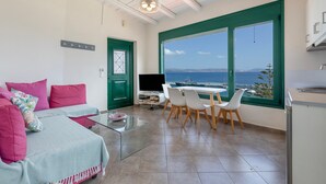 A modern living room with a sofa, a coffee table, and a dining area with chairs. There is a TV and a window with a view of the sea. - Apartment 'Two Bedroom  Sea View' with Sea View, Wi-Fi and Air Conditioning (Crete)
