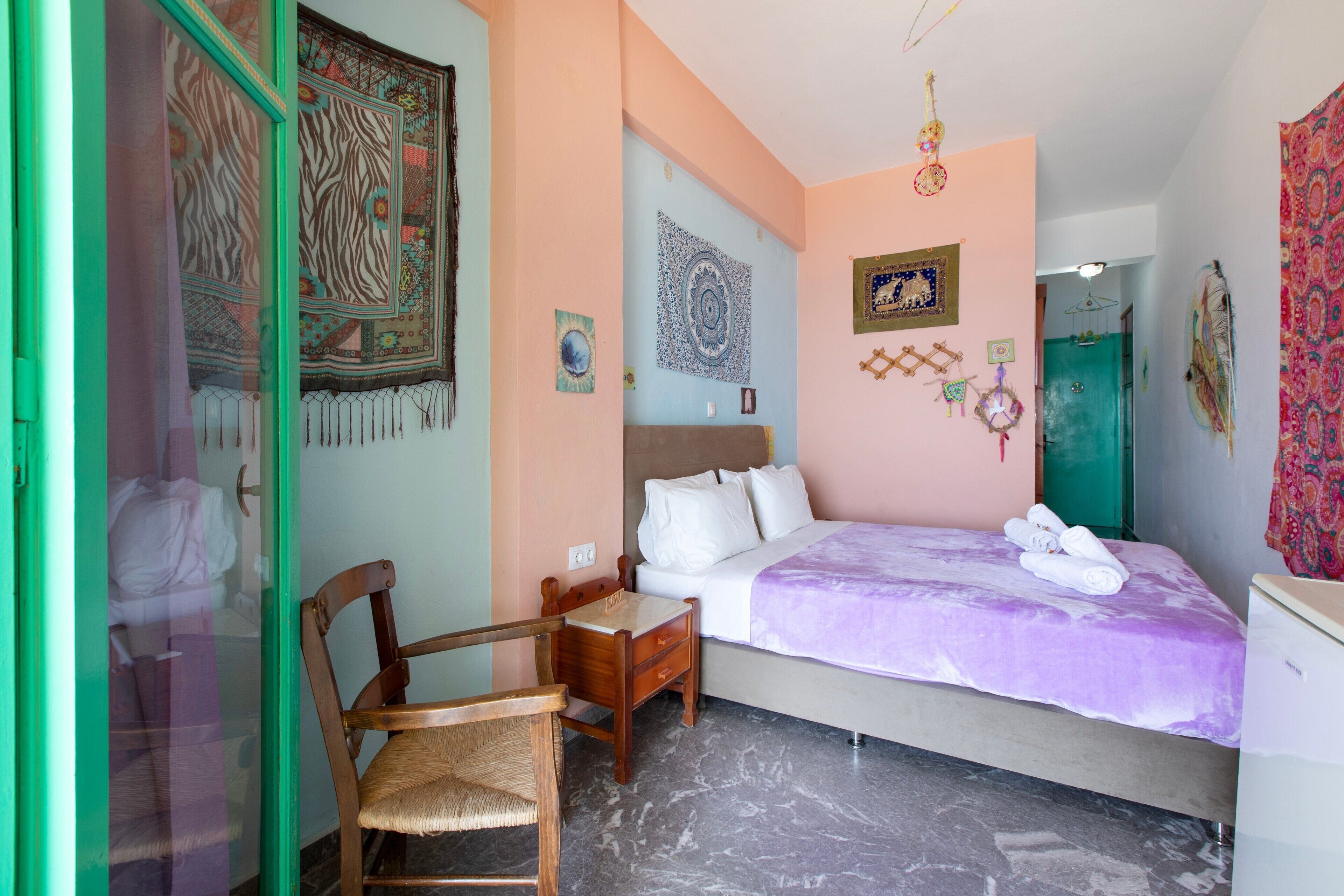 A bedroom with a bed, a chair, a desk, a wardrobe, and a door.