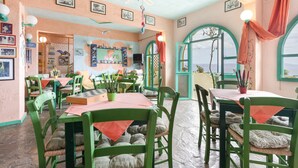 A dining area with green chairs, a table with a red tablecloth, and a ceiling fan. - Bed and Breakfast 'Double Room No 101 Sea View' with Sea View, Wi-Fi and Air Conditioning (Crete)