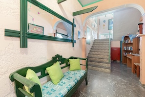 Un banco verde con cojines estampados, un espejo y una escalera con baldosas decoradas.