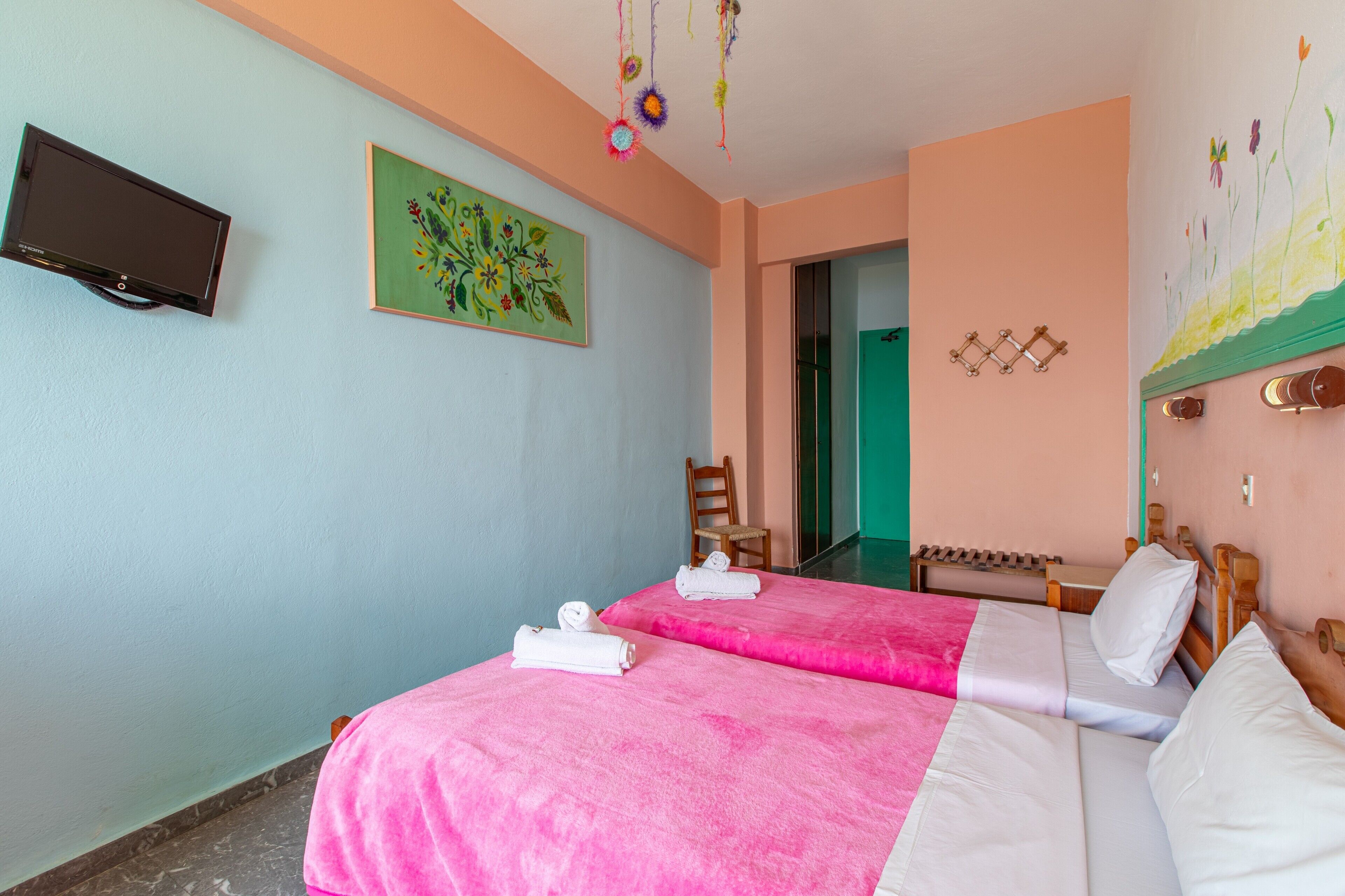 A hotel room with two beds, a television, a painting, and a wooden headboard.