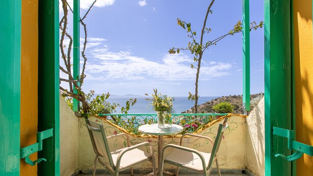 A balcony with a table and chairs, a vase with flowers, and a view of the sea. - Bed and Breakfast 'Double Room No 204 Sea View' with Sea View, Wi-Fi and Air Conditioning (Crete)