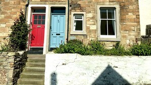 A two-story stone building with a red door and a blue door, numbered 29 and 27 respectively, and a small window labeled "BAYVIEW". - Bayview Townhouse | St Monans (St Monans)
