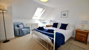 A bedroom with a bed, a chair, a bedside table, a lamp, and a radiator. - Bayview Townhouse | St Monans (St Monans)