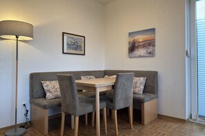 A corner room with a sofa, a table, and chairs, a lamp, and two framed pictures on the wall. - Bungalow mit Garten in Dornumersiel (Dornumersiel)