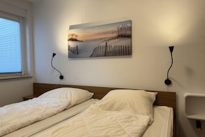 Ein Schlafzimmer mit zwei Betten, einem Wandbild, Nachttischlampen und einem Fenster mit Jalousien.