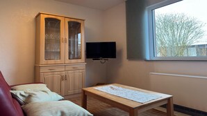 Una habitación con un armario de madera, un televisor, una ventana y una mesa.