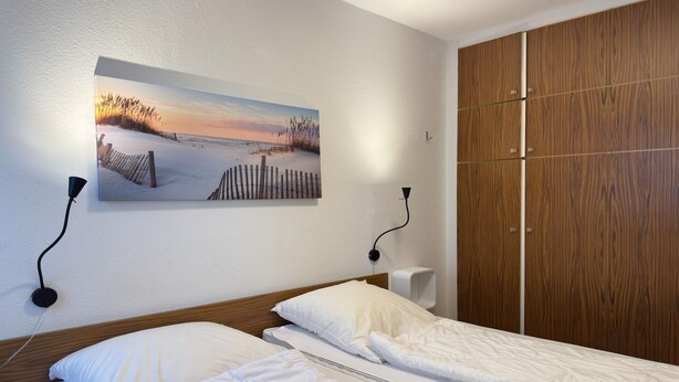Habitación de hotel con cama, un cuadro de una playa, armario de madera y un altavoz en la pared.
