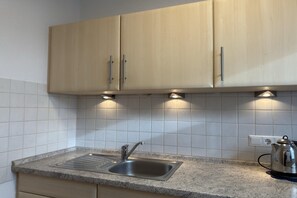 A kitchen with a stainless steel sink, wooden cabinets, and a kettle on the counter. - Bungalow mit Garten in Dornumersiel (Dornumersiel)