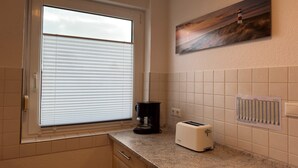 Una cocina con ventana, cafetera, tostadora y un cuadro en la pared.