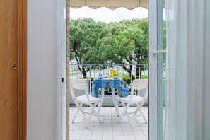 A balcony with a table and chairs, a view of trees, and a building in the background. - The Space🌴 Spacious Apartment in a Seafront Residence (the apartment has a street-side terrace) with Pool and Beach Spot – Experience the Best of Jesolo Lido! 🌊Description:Imagine waking up to the sound of the sea, having breakfast on a sunny ter (Lido di Jesolo)