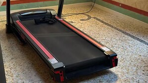 Un tapis de course dans une pièce dont le sol est recouvert d’un motif et un des murs est orné d’une bande verte et rouge.