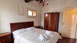 Un lit bien fait, avec du linge de lit blanc, une tête de lit en bois, une armoire en bois et un lustre.
