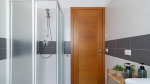 A modern bathroom with a glass-enclosed shower, a wooden door, and a shelf with toiletries. - ChatGPT ha detto:The SpaceWelcome to your corner of tranquility at the gateway to Venice!This cozy apartment in Mestre is the ideal solution for those who want to enjoy Venice stress-free, thanks to its strategic location in a quiet, safe, and well-serve (Venice)