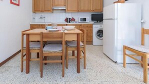 Een kleine keuken met houten kastjes, een witte koelkast, een magnetron en een wasmachine.