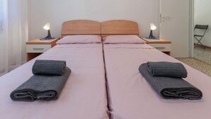 Een tweepersoonsbed met een houten hoofdbord, twee nachtkastjes met lampen en een opgevouwen handdoek aan elke kant.