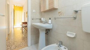 Een badkamer met een wastafel op een voetstuk, een wastafelmeubel met een spiegel, een toilet en een douchehoek.