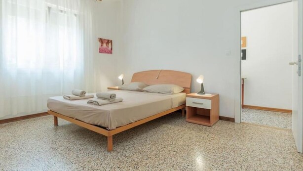 Een slaapkamer met een bed, nachtkastjes, een deur en een raam met gordijnen.