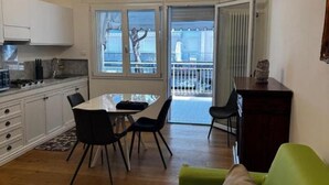 A modern kitchen with white cabinets, a dining table with chairs, and a view of the outside through large windows. - The Space🌟 Your Exclusive Retreat in the Heart of Jesolo – Comfort, Style, and an Unbeatable Location 🌟Imagine waking up with the scent of the sea in the air, having breakfast on a private terrace overlooking Jesolo’s famous walking street, and (Lido di Jesolo)