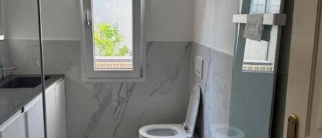 A compact bathroom with a toilet, bidet, and a window.