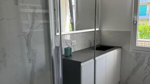 A modern bathroom with a glass shower enclosure, a white sink with a black countertop, and a view of greenery outside. - The Space🌟 Your Exclusive Retreat in the Heart of Jesolo – Comfort, Style, and an Unbeatable Location 🌟Imagine waking up with the scent of the sea in the air, having breakfast on a private terrace overlooking Jesolo’s famous walking street, and (Lido di Jesolo)