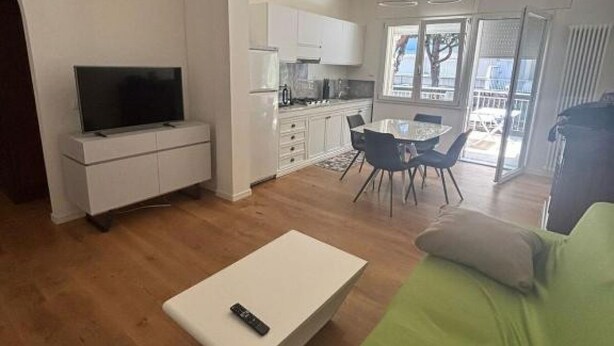 A modern living room with a flat-screen TV on a white cabinet, a dining area with a table and chairs, and a green sofa. - The Space   🌟 Your Exclusive Retreat in the Heart of Jesolo – Comfort, Style, and an Unbeatable Location 🌟Imagine waking up with the scent of the sea in the air, having breakfast on a private terrace overlooking Jesolo’s famous walking street, and (Lido di Jesolo)