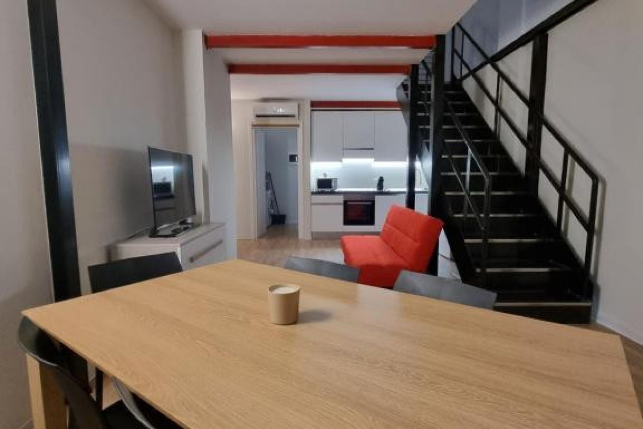A modern living space with a dining area, a kitchen, and a staircase.