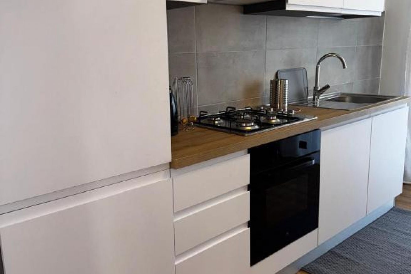 A modern kitchen with white cabinets, a wooden countertop, a built-in oven, and a stainless steel sink.