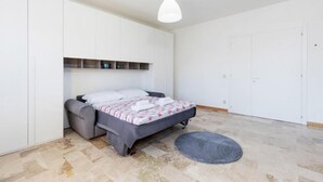 A bedroom with a bed, a grey sofa, a white wardrobe, a hanging light fixture, and a small rug. - The SpaceLooking for a comfortable, stylish, and strategically located stay to explore Venice and beyond? This newly renovated home in Mestre is the ideal solution for families, small groups, and travelers seeking both comfort and convenience.Just steps  (Venezia)
