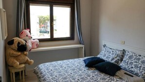 A bedroom with a bed, a window with curtains, and two stuffed animals on a shelf. - The SpaceSpacious, comfortable, and bright apartment located near Jesolo beach and the famous Caribe Bay water park.The house enjoys a super strategic position, allowing you to make the most of everything Jesolo Lido has to offer.The apartment can host u (Lido di Jesolo)