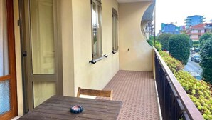 A balcony with a table and chairs, a view of the street, and a building with a curved roof. - Sottomarina - House Near Sea | Terrace & Private Garage (Chioggia)