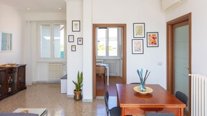 Une pièce spacieuse avec une table à manger en bois, des chaises, une plante en pot et des œuvres d’art encadrées accrochées aux murs.