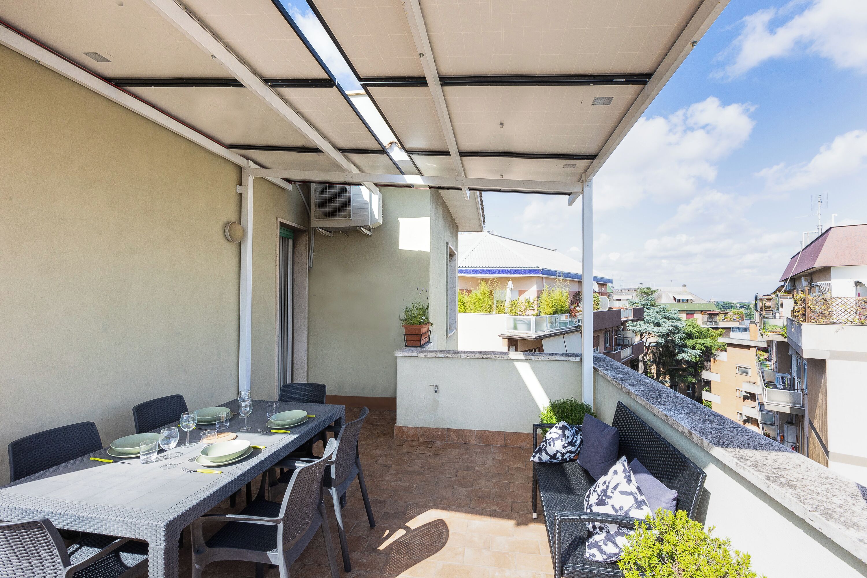 Een balkon met een eettafel, stoelen en een bank met kussens.